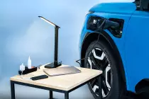 focused-shot-of-micras-charging-port-with-v2l-connected-to-an-extension-where-a-laptop-iphone-and-lamp-is-charging-on-a-coffee-table